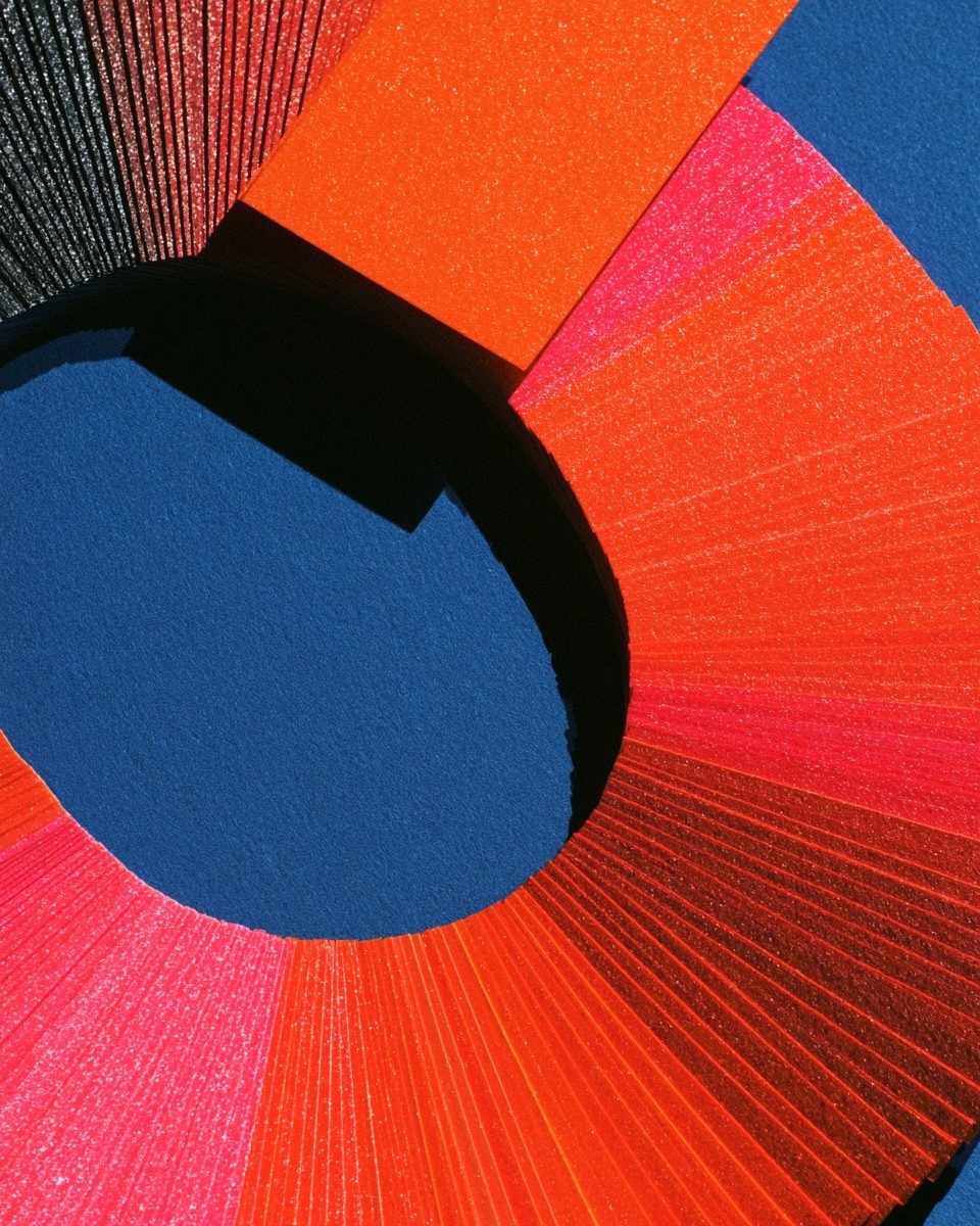 Sheets of red, orange and blue paper fanned into a ring in hard sun